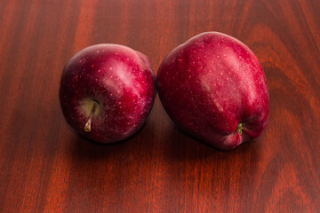 Two dark red apples on a dark wooden table
