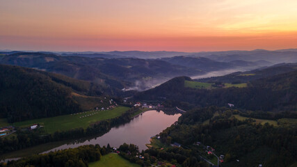 Aerial view of a hill on the Bystricka dam and the surrounding hills during sunset between the valley appears fog.