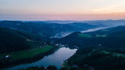 Aerial view of a hill on the Bystricka dam and the surrounding hills during sunset between the valley appears fog.
