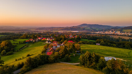 Aerial landscape view at orange sunset with field and village lying in the background.