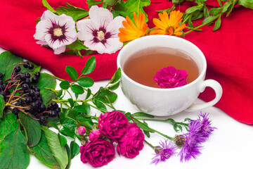 Herbal tea of fresh rose, dog-rose, cornflowers, mallows and calendula flowers on white background. Cup of flower tea and ingredients. Herbal medicine concept
