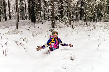 Fototapeta na wymiar A happy cheerful girl climbed into a snowdrift on a walk outside the city in the forest.