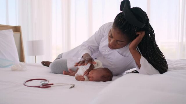 African American woman doctor also act as mother sing baby to sleep on bed in bedroom and touch baby for relax and feel safe with children healthcare concept.