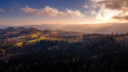 Aerial view of hilltops during sunrise rays shine through the landscape through clouds on the ground during the autumn morning Beskydy region.