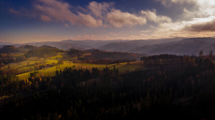 Aerial view of hilltops during sunrise rays shine through the landscape through clouds on the ground during the autumn morning Beskydy region.