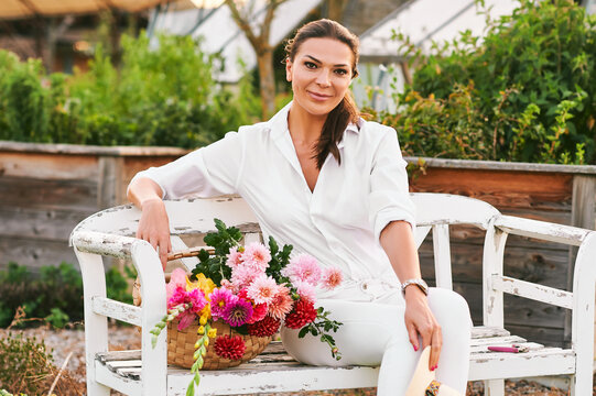 Happy And Healthy Gardener Woman Resting On Bench With Basket Full Of Colorful Flowers, Hobby And Leisure, Nature Lifestyle