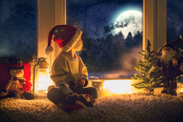 Cute child, sitting on a window, looking outdoors for Santa Claus