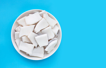 Coconut cut pieces in bowl on blue background.