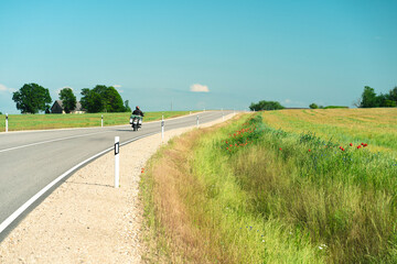 Asphalt road between agricultural fields of Latvia. Sunny summer bright day.