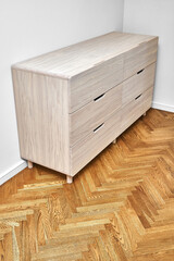 Elegant chest of drawers made with bleached solid oak timber with finger pull drawers stands on wood block parquet floor in light room