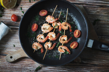 
Shrimp shashlik in a pan, fried in oil and with spices. All this is on the table. Nearby is a plate of shrimp shashals