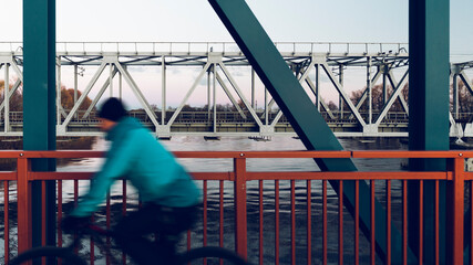 Cyclists and passers-by on the pedestrian bridge across the river next to the railway on a sunny spring day