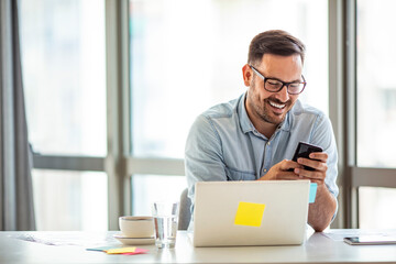 Head shot young businessman sitting at table with computer, working remotely, writing email or...