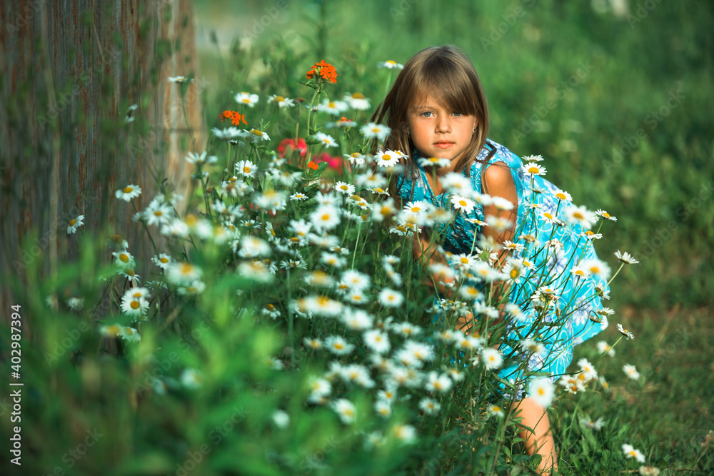 Wall mural A little girl posing in the yard of a country house among flowers.