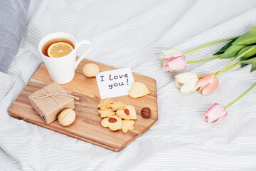 Festive breakfast in bed for Valentine's Day. Tea and cookies with your own hands in the form of hearts. A note on paper, a gift and flowers to your beloved girl