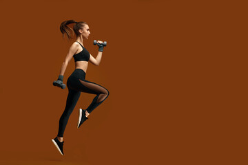 Fototapeta na wymiar athletic beautiful woman in black sportswear training with dumbbells isolated on yellow background. girl jumping with dumbbells. sport and fitness concept. copy space