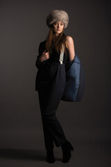 beautiful girl in a black trouser suit and a fur hat on her head posing in the studio on a dark gray background