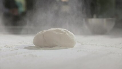 Young chef works as baker in restaurant's kitchen. man sprinkles raw dough with wheat flour on table for making traditional national pizza. Preparation of ingredients for making pizza dough.