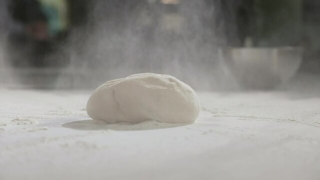Young chef works as baker in restaurant's kitchen. man sprinkles raw dough with wheat flour on table for making traditional national pizza. Preparation of ingredients for making pizza dough.