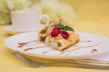 Roll with cottage cheese and raspberries poured with soft caramel on a white ceramic plate.