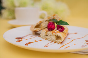 Roll with cottage cheese and raspberries poured with soft caramel on a white ceramic plate.