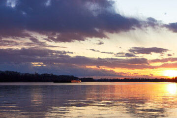 Obraz premium Landscape view of the river in the evening time, with wonderful blue cloudy sky during the yellow sunset lighting and a barge (ship) on the horizon