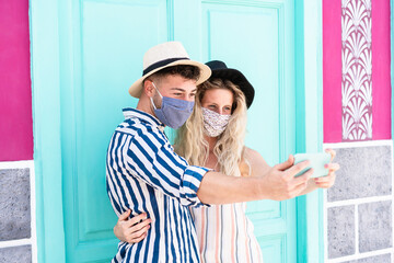 Young couple taking selfie with safety masks outdoors during coronavirus outbreak - Main focus on man