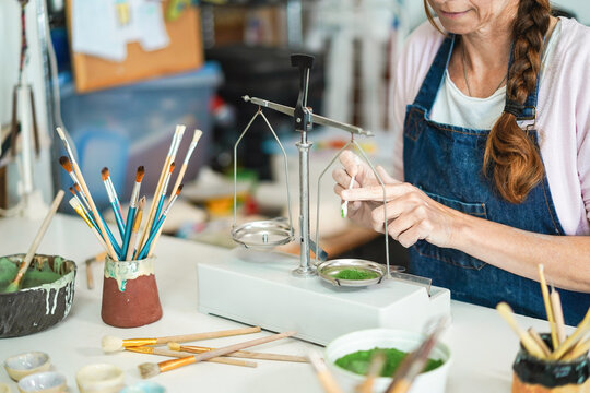 Artist woman mixing painting colors with vintage balance at pottery workshop studio -