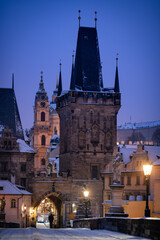 Fototapeta premium Lesser Town Bridge Tower during the moody winter night. Romantic scene before the sunrise with the snow and illuminated lamps.