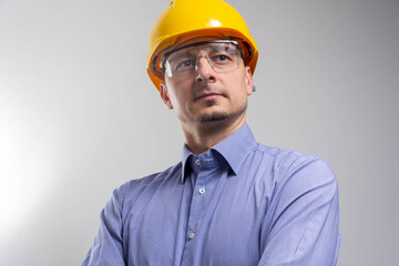happy smiling construction engineer with hands crossed wearing yellow helmet on grey background. 