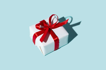 Holiday present. Women day surprise. Homemade gift. Special occasion congratulation. Wrapped white box with red ribbon bow isolated on blue empty space background.