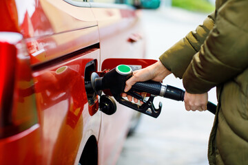 Close-up of hands of woman at self-service gas station, hold fuel nozzle and refuel the car with...