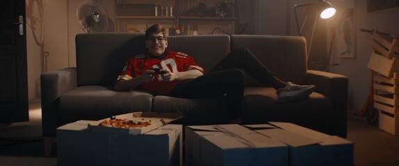 POV Portrait of Caucasian teenager playing video game inside home garage, enjoying pizza. Shot with 2x anamorphic lens