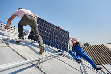 Male team workers installing stand-alone solar photovoltaic panel system. Electricians mounting blue solar module on roof of modern house. Alternative energy sustainable environmental ecology concept.