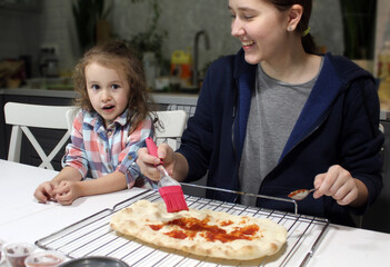 The teenager and the little girl is smeared with a brush of tomato sauce pizza dough