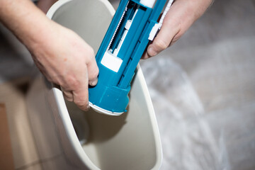 Obraz premium A plumber installs a water pump in a ceramic toilet cistern. Drain system assembly, home repair.