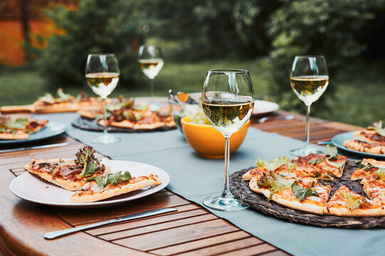 Dinner in a home garden. Pizza, salads, fruits and white wine on table in a orchard in a backyard