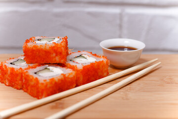 Sushi maki rolls with chopsticks on bamboo table with soy sauce.