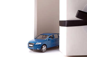 Photo of toy blue suv fashionable car driving out of white present box with big black  bow isolated over white background. 
Gift, win or victory concept