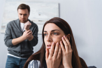 Woman cheek with bruise near abusive husband showing fist on blurred background