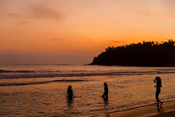 Three friends entering the sea at sunset