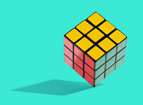 Colourful Rubiks Cube balanced on edge on cyan background