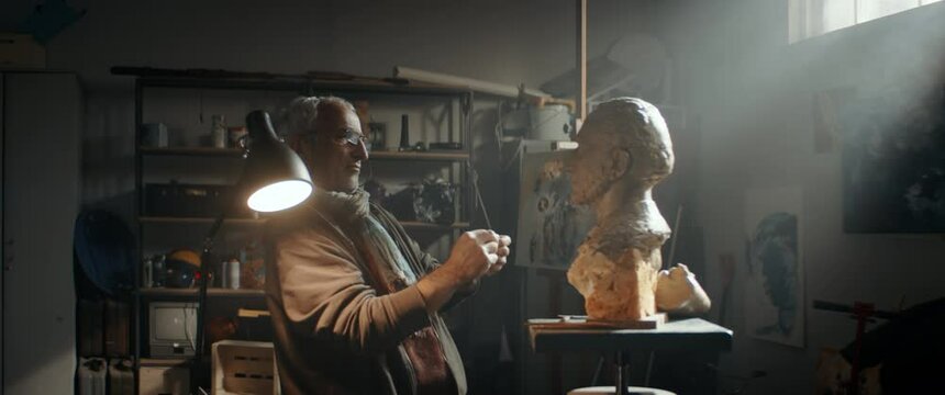 WIDE to MED Portrait of senior adult middle eastern male sculptor working on a bust project in his home garage workshop. Retirement hobby concept. Shot with 2x anamorphic lens