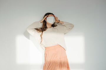 Denier woman in a white sunlit room with a white fabric mask on her face. Leaning back, holding her...