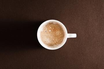 White cup with coffee on brown background. Flat lay, top view, copy space.