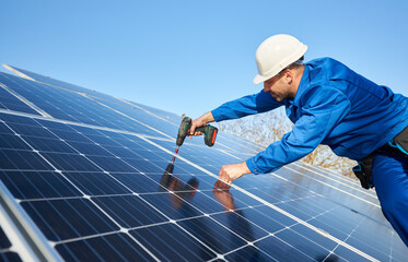Male engineer in blue suit and protective helmet installing stand-alone solar photovoltaic panel...