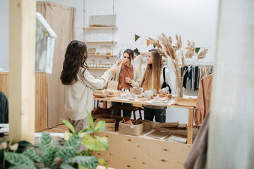 Longshot of three curious young women in an ecological shop choosing between various cosmetic products. Standing in front of the table with variety of items. One is inhaling aroma.
