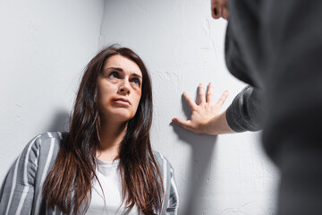 Woman with bruises on looking at abuser on blurred foreground near walls
