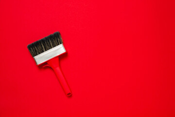 Large new red brush in metal edging with plastic handle for construction painting or canvas priming on a red background. Christmas banner with copy space for a hardware store or art shop. Close-up