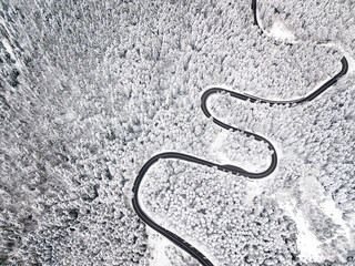 Winding road among a snowy forest, from high mountain pass, winter weather. Aerial view by drone. Romania